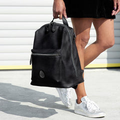 Woman legs holding a Hartland Pack black backpack by her side