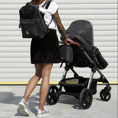 Woman pushing a pram with the Hartland Pack Black worn as a backpack