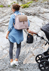 Woman on a rocky beach wearing the hastings latte backpack and holding on to a pram