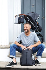 Man sitting on a step with the Picos Carbon backpack at his feet and a pram behind him