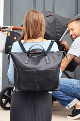 The back of a woman wearing the Saunton black as a backpack looking at a man in front of her with a pram