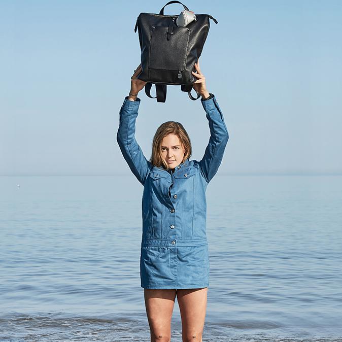 Woman walking along the beach wearing the black backpack and holding the pods in her hand