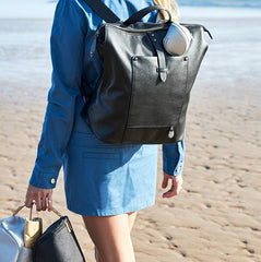 Woman walking along the beach wearing the black backpack and holding the pods in her hand